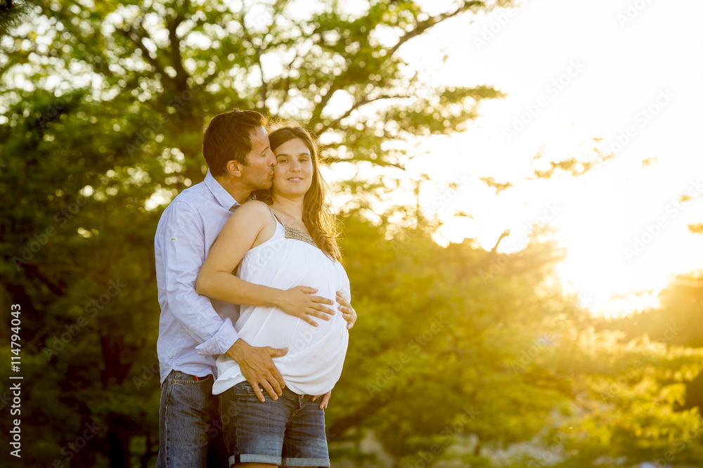 Fototapeta premium happy couple in love together in park landscape on sunset with woman pregnant belly and man