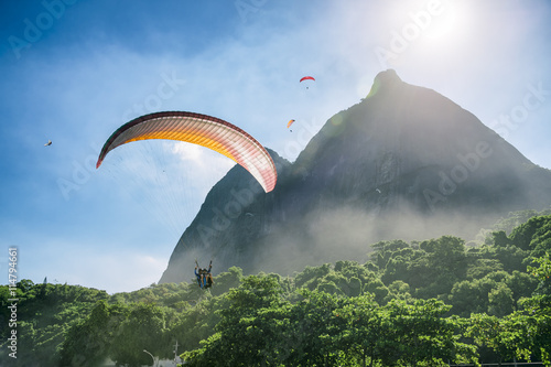 Paraglider passes along the misty greenery of Pedra da Gavea Mountain on its way to land at São Conrado Beach in Rio de Janeiro, Brazil