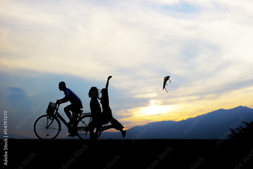 children enjoy flying a kite with ride bicycle during sunset.