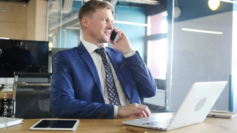 Successful young businessman talking on smart phone in office Successful young businessman talking on smart phone in office