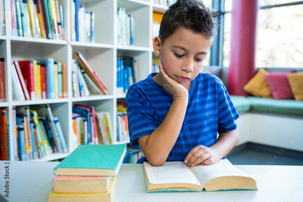 Elementary boy reading book in school library Elementary boy reading book in school library