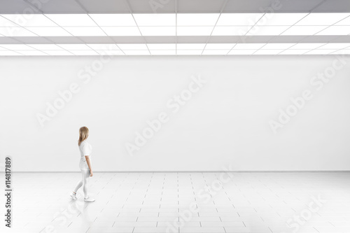 Empty big hall wall mockup. Woman walk in museum gallery with blank wall. White clear stand mock up lobby. Display artwork presentation. Art design empty floor. Expo studio wall in loft corridor.