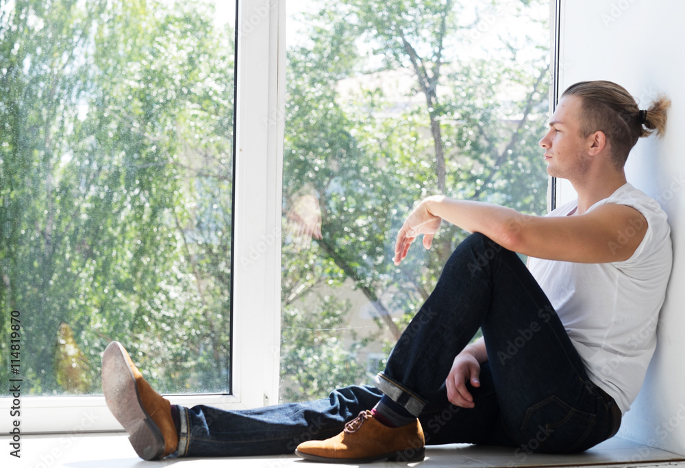 Handsome young man sitting on windowsill 