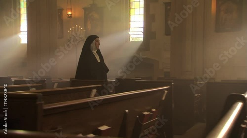 Nun walking slowly up aisle of Catholic church, votive candles in foreground photo