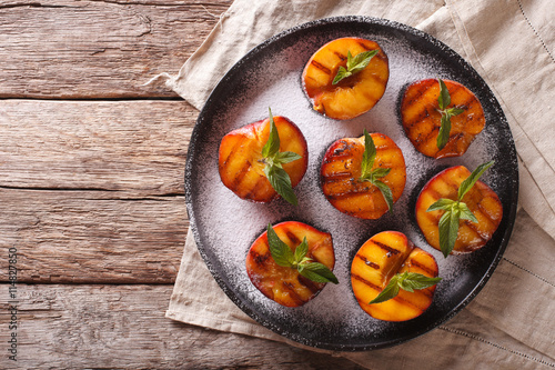 Ripe peaches grilled with powdered sugar and mint on a plate. horizontal top view
