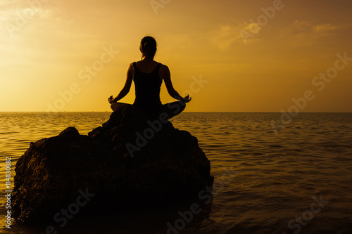 Silhouette of woman practicing yoga on the rock during a beautif