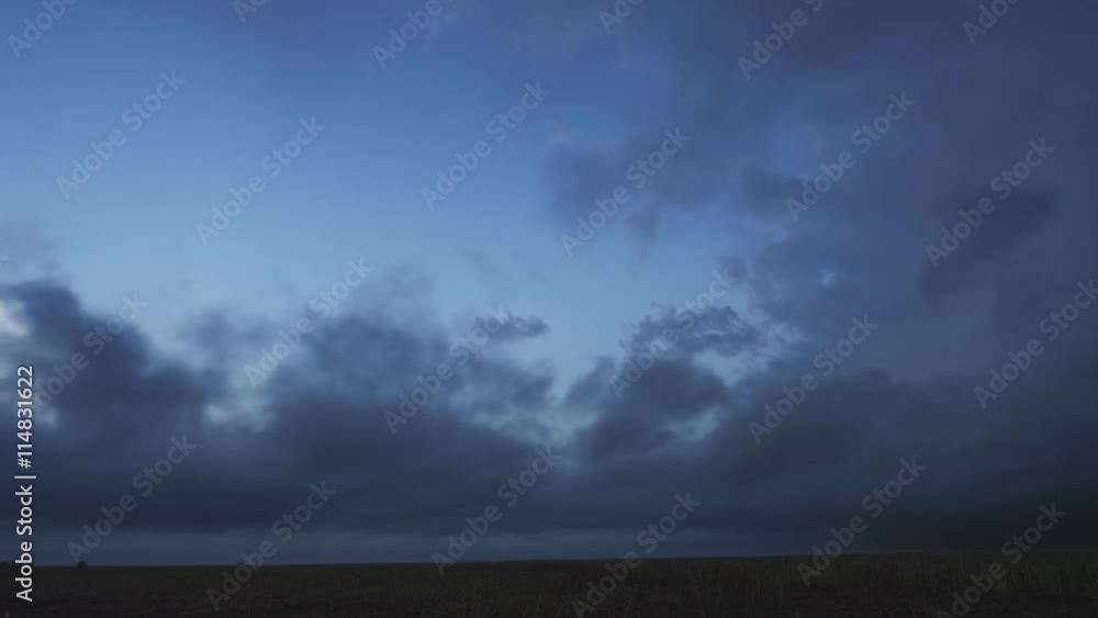 Low ragged time-lapse clouds blow across the prairie at evening as a column of cloud rises at right