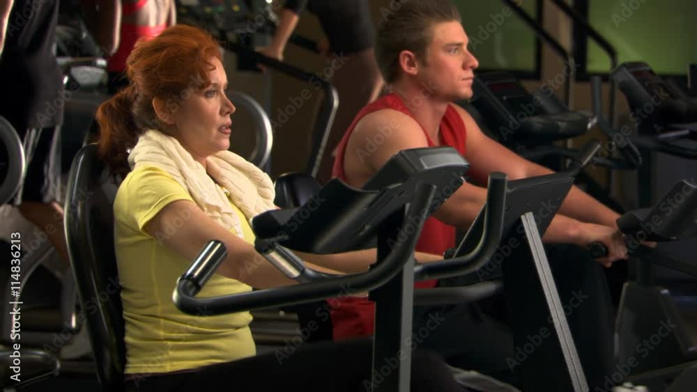 Man and woman pedaling recumbent stationary bikes in health club Man and woman pedaling recumbent stationary bikes in health club