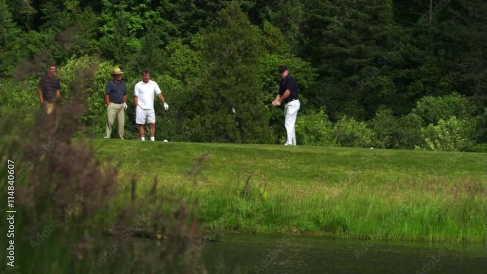 Foursome at water hazard, one golfer hitting ball into water Foursome at water hazard, one golfer hitting ball into water