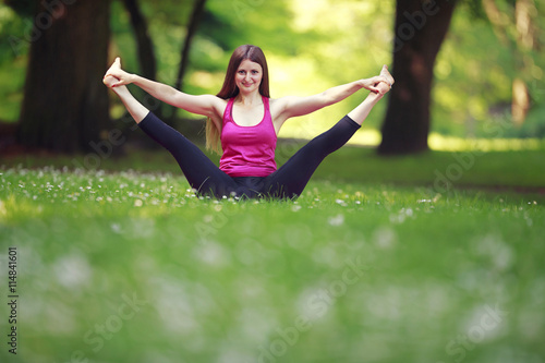 Young woman doing yoga exercises in park's lawn. Girl in pink sport wear sitting in yoga pose in the park.