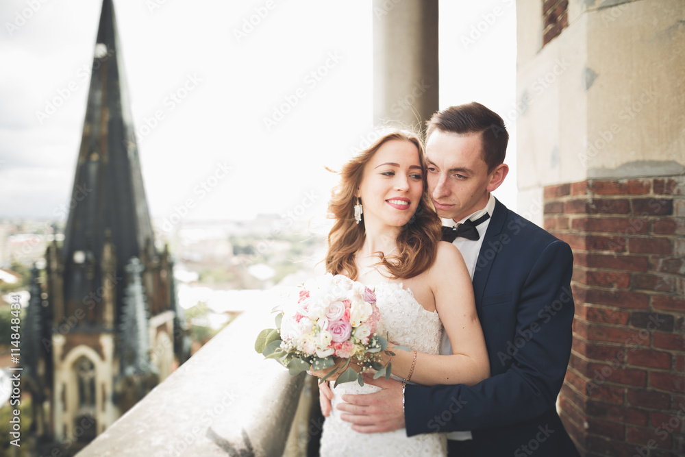 © olegparylyak - Stylish beautiful wedding couple kissing and hugging on background panoramic view of the old town © olegparylyak - Stylish beautiful wedding couple kissing and hugging on background panoramic view of the old town