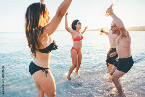 group of young multiethnic friends women and men at the beach in summertime jumping and dancing in back light - happiness, friendship, together concept