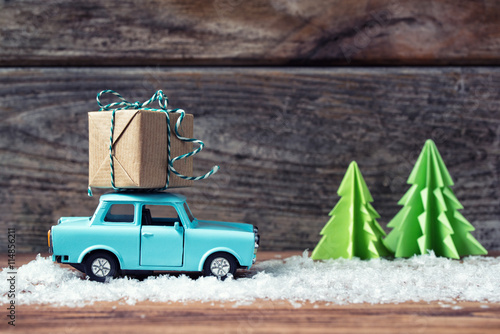 Toy car carrying a Christmas gift with snow and paper fir trees