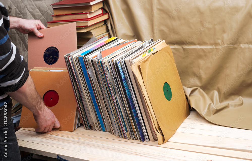 Obraz premium Retro styled image of a collection of old vinyl record lp's with sleeves on a wooden background. Browsing through vinyl records collection. Music background. Copy space