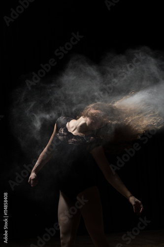 Woman dancing with flour in hair. Black background.