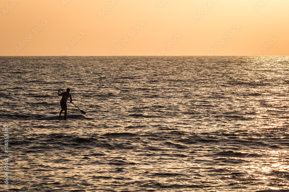 Silhouette of a young man on his sup paddle board during a clear sunset