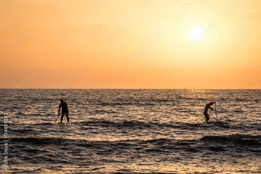 Silhouettes of 2 young men on their sup paddle board during a clear sunset