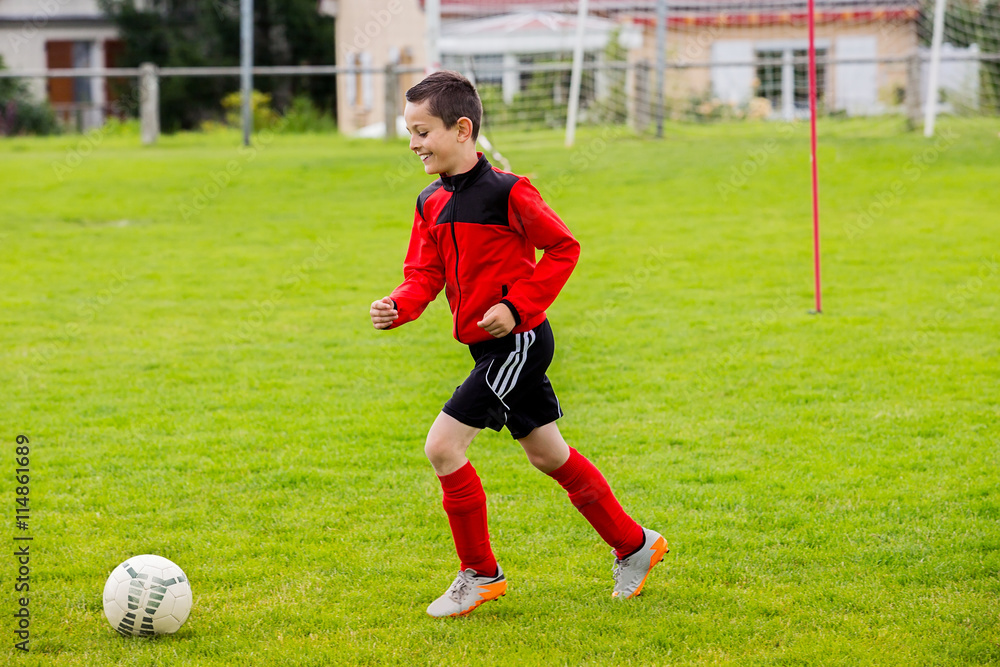 Little Boy playing soccer on the sports field.Training little boy on a asport field.Boy running with a soccer ball on a country sport field .