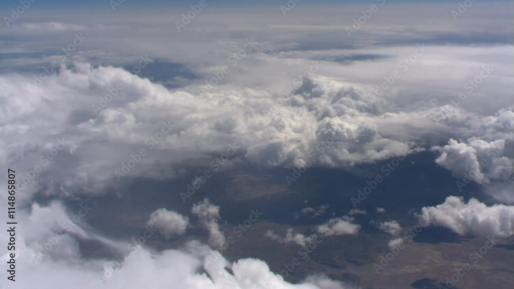 Flight over billowing cloud masses with arid terrain below Flight over billowing cloud masses with arid terrain below