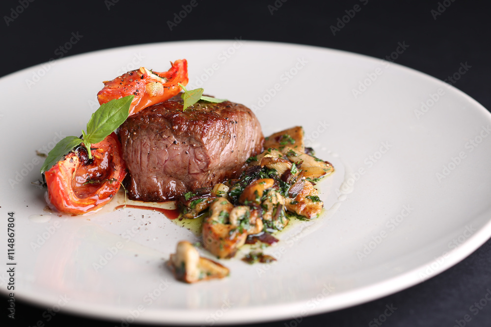 Roasted meat with tomatoes and mushrooms on a white plate, dark background in the restaurant