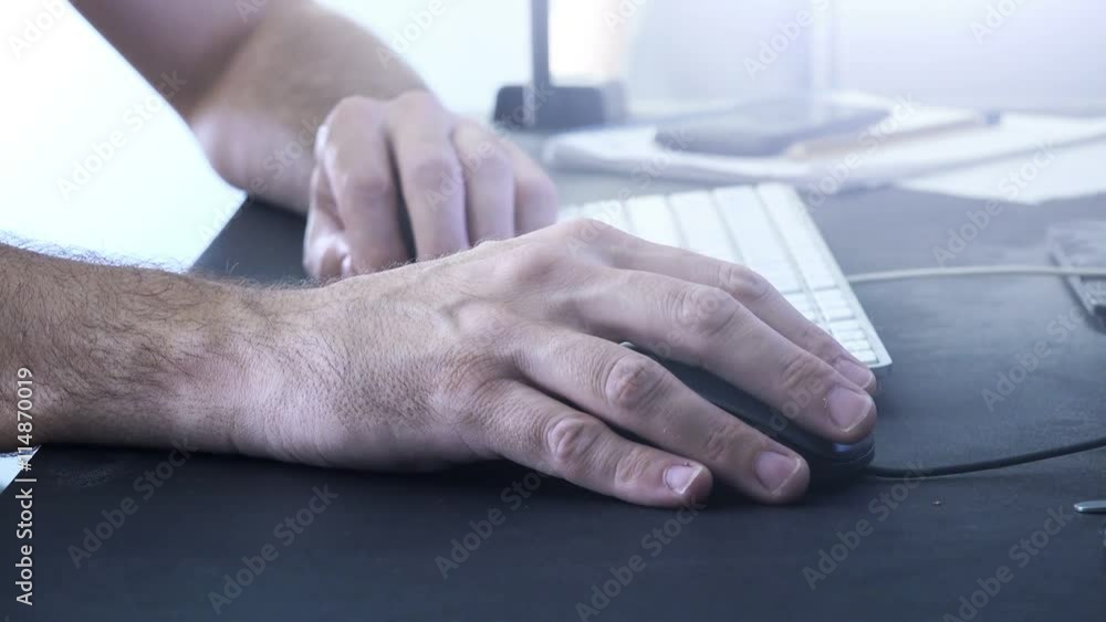 Male hand with computer mouse at office desk, man working on desktop pc Male hand with computer mouse at office desk, man working on desktop pc