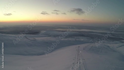 Aerial view of Khibiny mountains, Russia in twilight. There is a ski-lift on the slope, man is driving the snowmobile photo