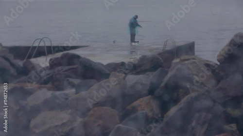 the lonely fisherman on a stone pier in rainy weather catches fish photo