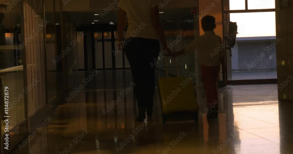 Mother and son walking and rolling a suitcase together at the airport terminal Mother and son walking and rolling a suitcase together at the airport terminal
