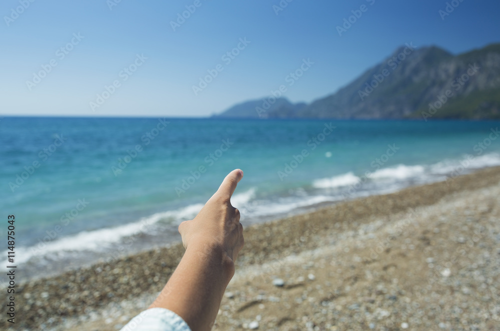 Female hand pointing to the sea landscape with mountains, out of focus