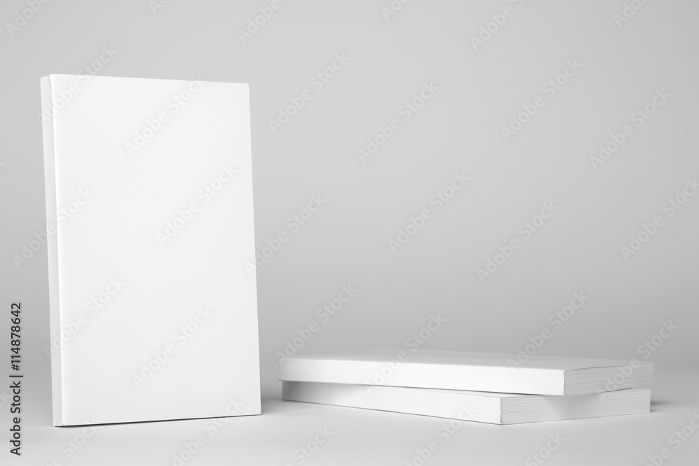 Naklejka premium Real paperback white book next to a stack of books on a gray 
