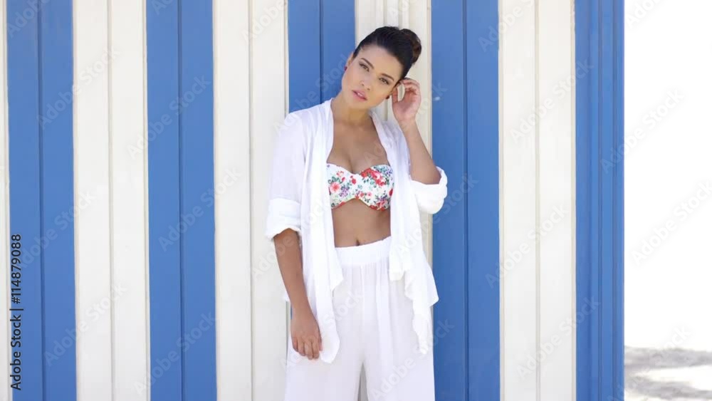 Pretty single woman with tied back hair and hands on hip wearing robe while leaning against blue and white wall outdoors Pretty single woman with tied back hair and hands on hip wearing robe while leaning against blue and white wall outdoors