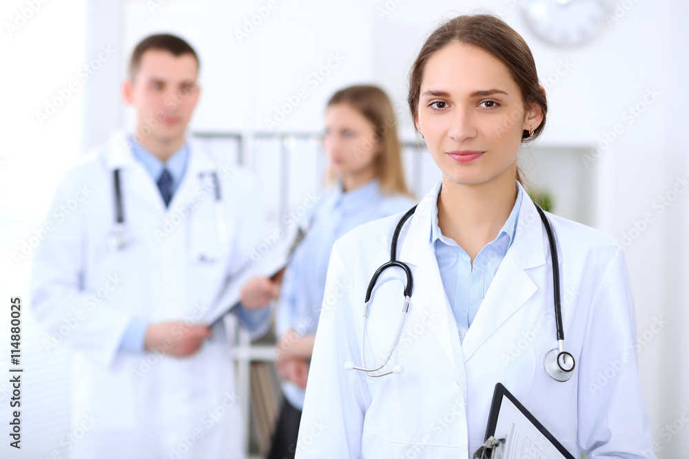 Young beautiful female doctor smiling on the background with patient and his doctor in hospital. High level and quality medical service concept. Young beautiful female doctor smiling on the background with patient and his doctor in hospital. High level and quality medical service concept.
