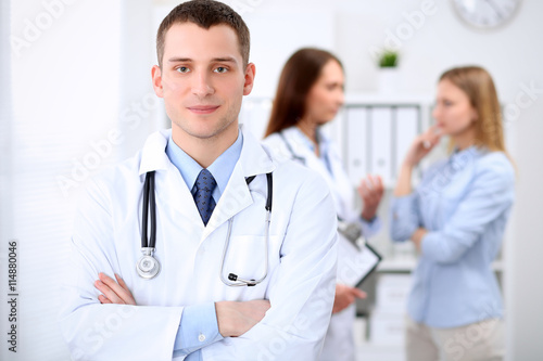 Friendly male doctor  on the background with patient and his doctor in hospital. High level and quality medical service concept.