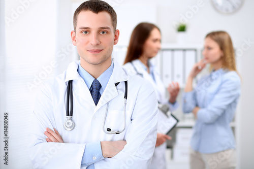 Friendly male doctor on the background with patient and his doctor in hospital. High level and quality medical service concept.