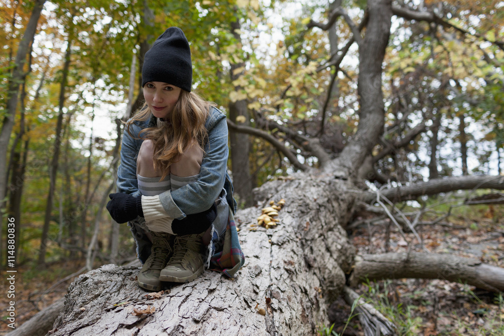 Portrait of young woman sitting on tree trunk in forest Portrait of young woman sitting on tree trunk in forest