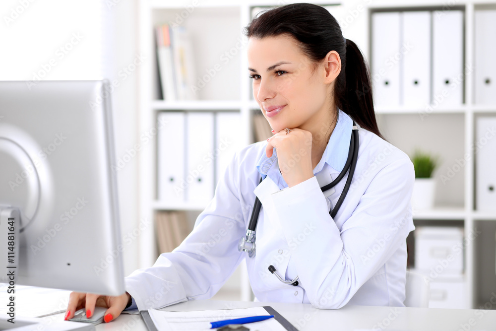 Young brunette female doctor sitting at the table and working by computer at hospital office. Doctor is in trouble with diagnosis. Health care, insurance and help concept. Young brunette female doctor sitting at the table and working by computer at hospital office. Doctor is in trouble with diagnosis. Health care, insurance and help concept.