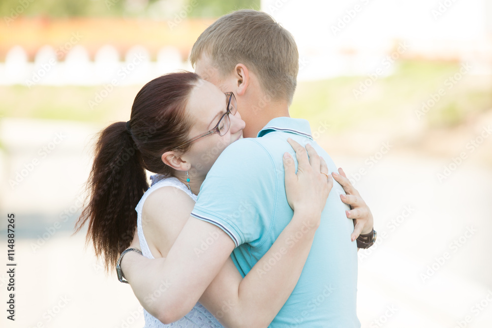 Beautiful young romantic couple in relationship meeting or parting on the street and hugging each other tightly with affection. Two people in love embracing in summer park