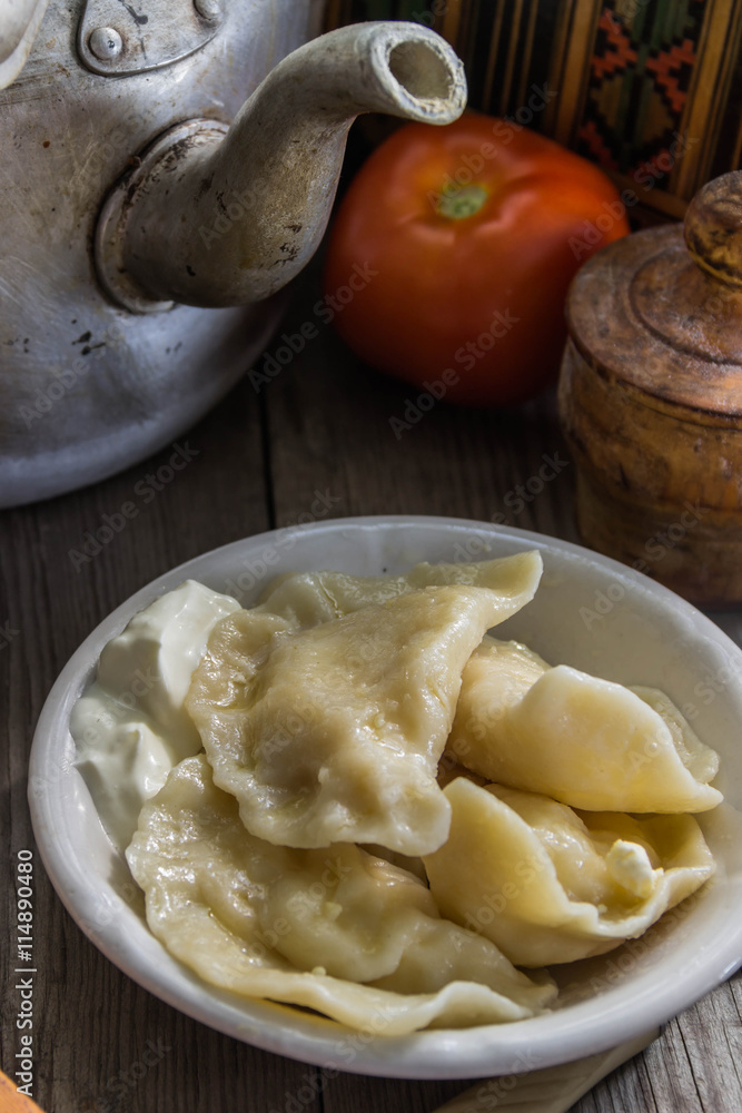 Traditional Ukrainian and Russian cuisine , dumplings called varenyky of dough with cottage cheese and sour cream in a clay plate with national attributes on a wooden background Traditional Ukrainian and Russian cuisine , dumplings called varenyky of dough with cottage cheese and sour cream in a clay plate with national attributes on a wooden background