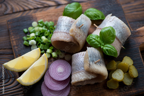 Herring rollmops with red and green onion, gherkins and lemon photo