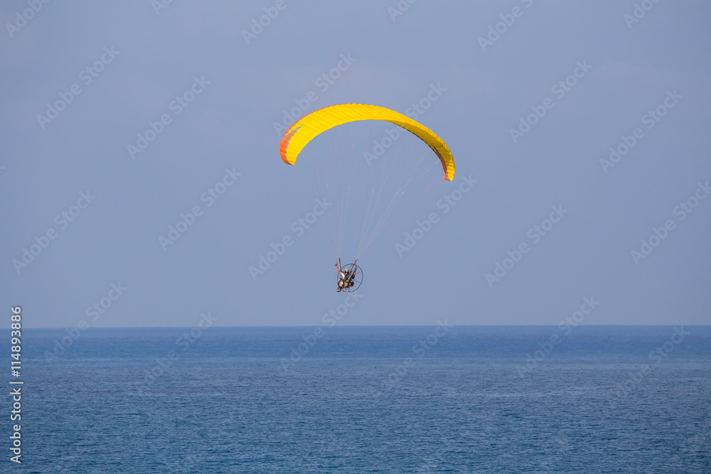 A yellow-orange propelled paraglider in a low flight over the sea A yellow-orange propelled paraglider in a low flight over the sea