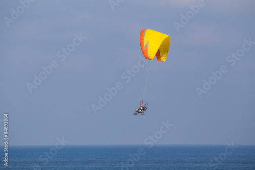 A yellow-orange propelled paraglider in a low flight over the sea