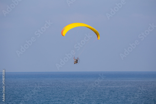 A yellow-orange propelled paraglider in a low flight over the sea