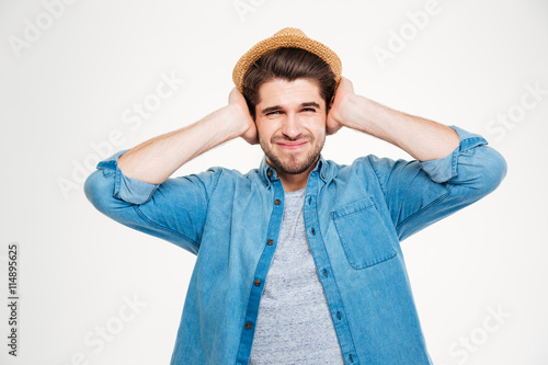 Frowning handsome young man covered ears by hands