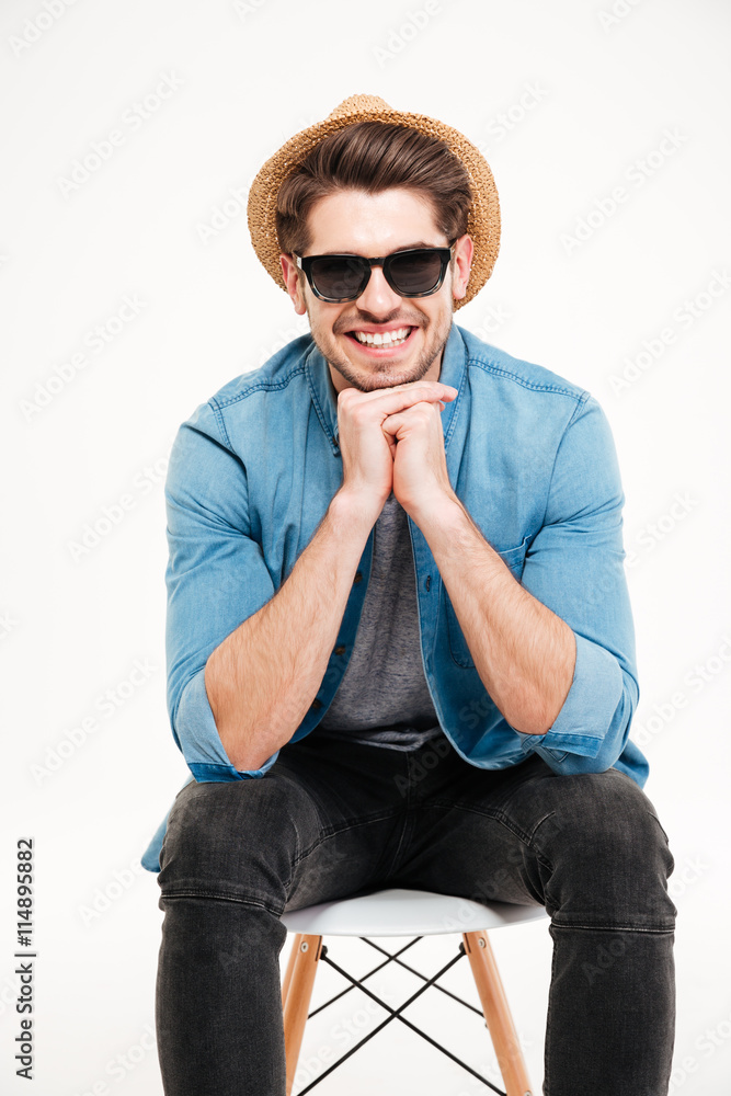 Happy young man in sunglasses sitting on chair and smiling Happy young man in sunglasses sitting on chair and smiling