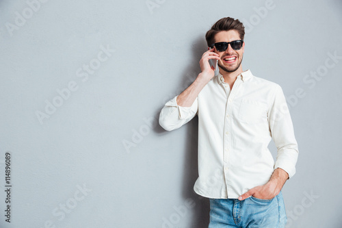 Cheerful confident young man in sunglasses talking on cell phone
