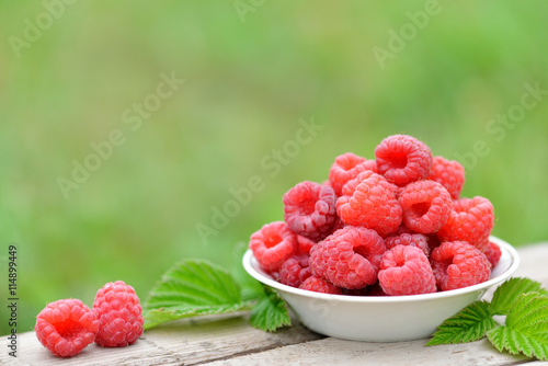 Fresh red raspberries on plate on blurred natural background