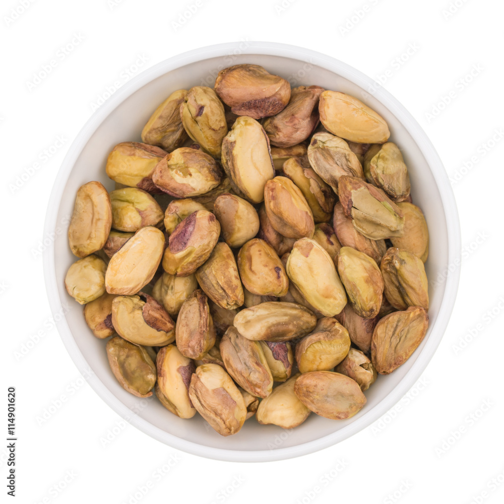At the center of the frame white bowl with raw pistachio kernels At the center of the frame white bowl with raw pistachio kernels