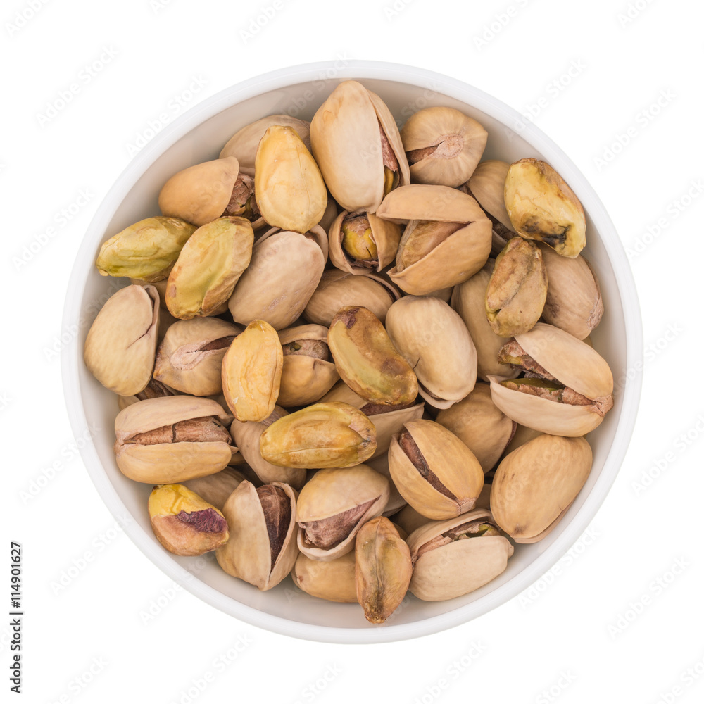 At the center of the frame white bowl with pistachio nuts on a w At the center of the frame white bowl with pistachio nuts on a w