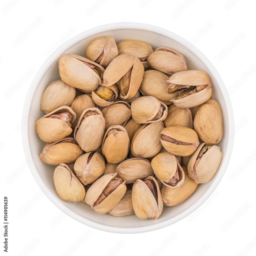 At the center of the frame white bowl with pistachio nuts on a w At the center of the frame white bowl with pistachio nuts on a w
