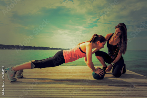 Jeune femme avec un coach sportif faisant des pompes sur un ballon en extérieur